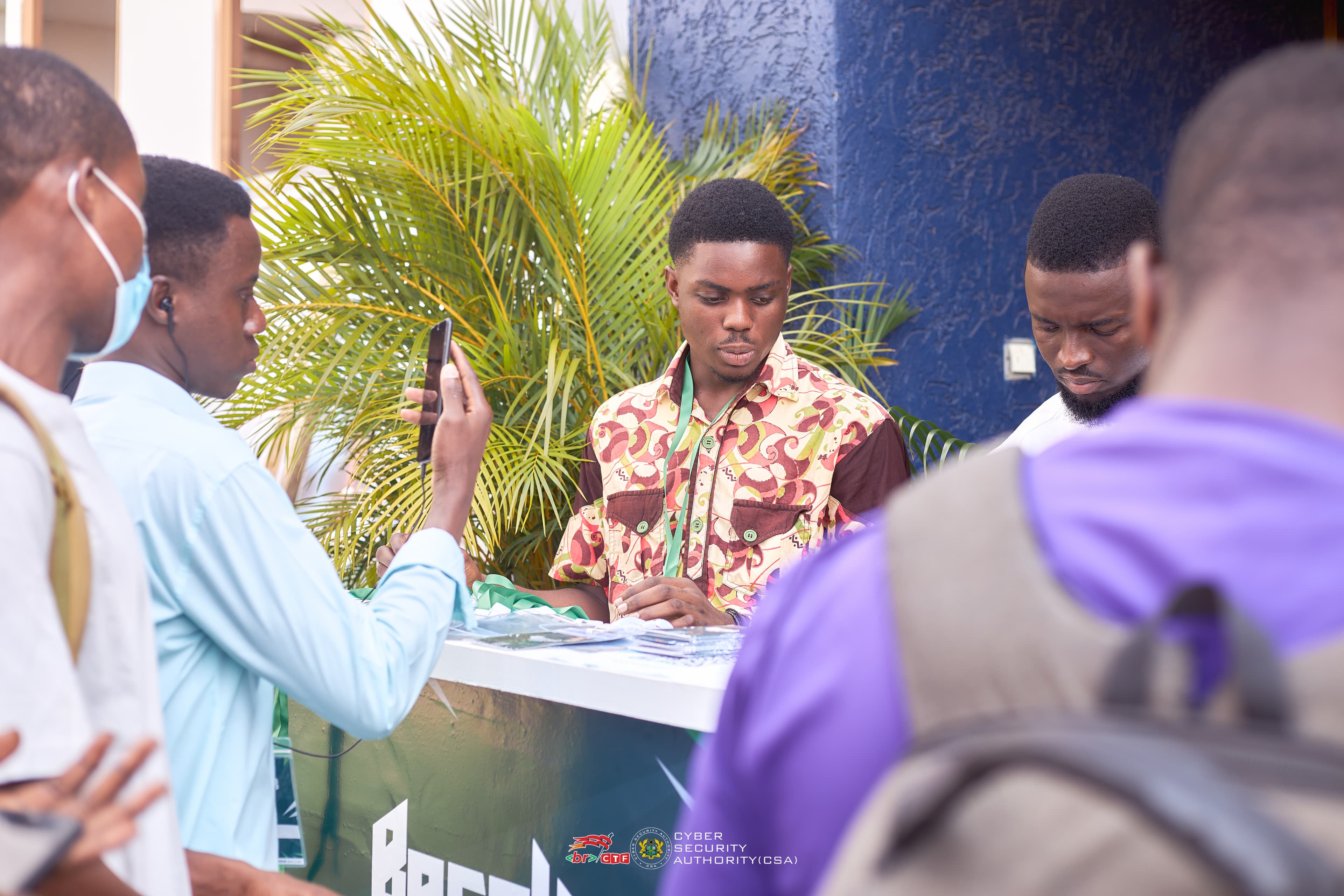 Friendly behind-the-scenes photo of organizers assisting attendees at a help desk while others network nearby.